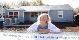 an image of a woman standing outside a house leaning against the chainlink fence surrounding the yard